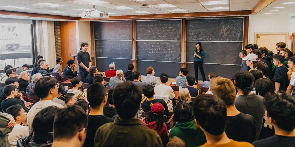 纽约大学柯朗数学、计算与数据科学学院数学系副教授王虹在黑板前授课,吸引众多研究生学生围观,体现数学博士与硕士项目的学术氛围和教学实力。
