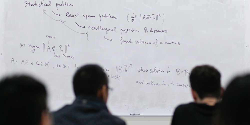 多名学生在纽约大学柯朗数学、计算与数据科学学院数学博士课程教室内认真聆听高等数学讲解,白板上写有数学公式,体现该博士项目的数学研究深度和严谨学术氛围。